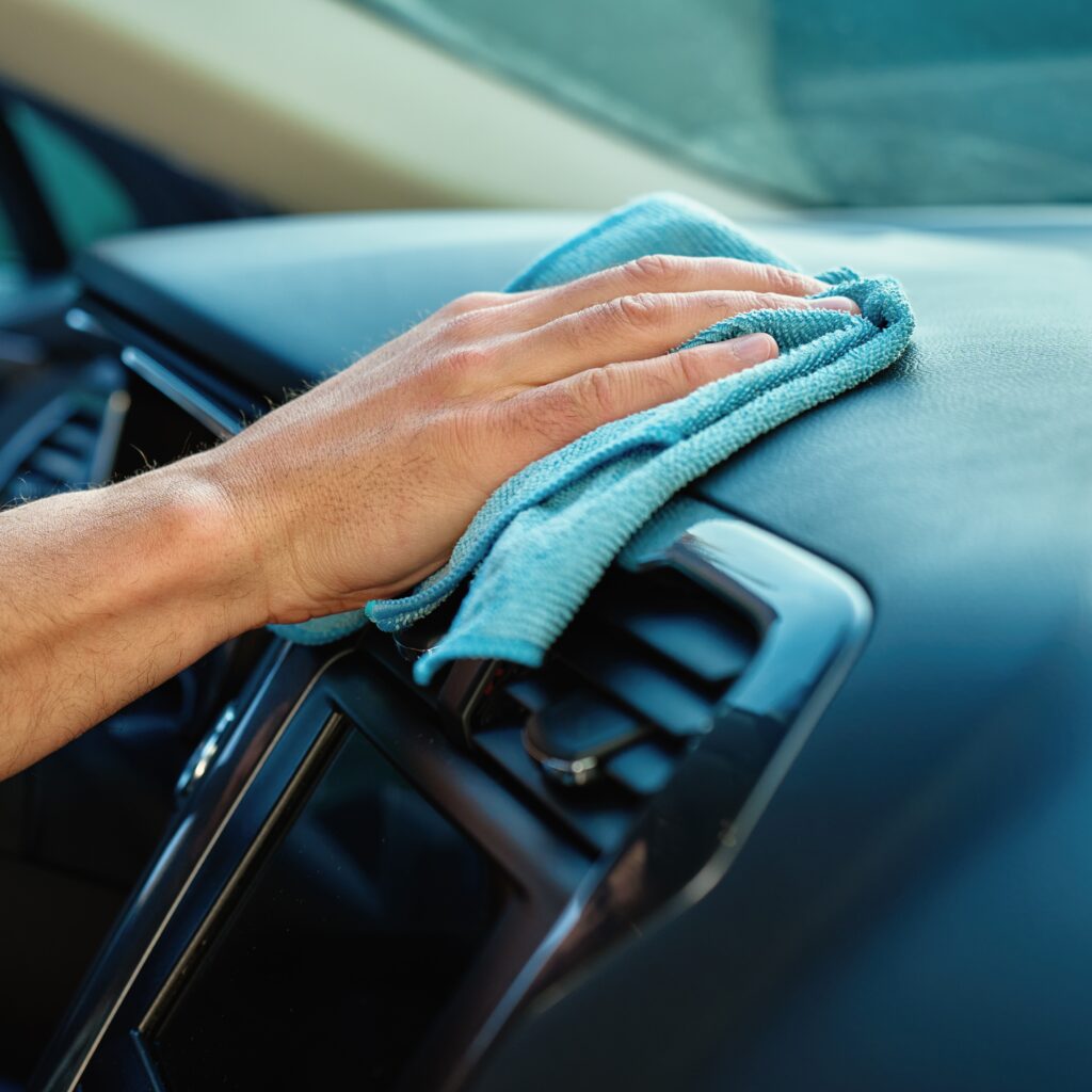 Close-up of male hand wiping car dashboard with microfiber cloth for cleaning. Concept of vehicle hygiene, interior maintenance and car detailing
