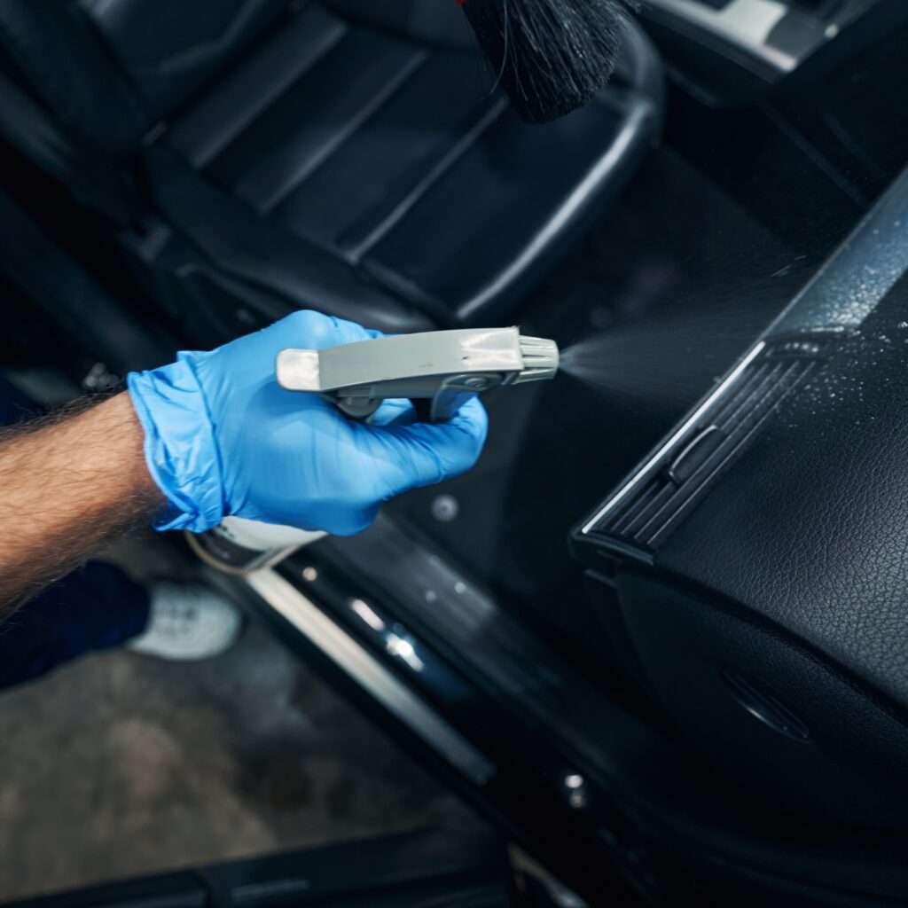 Car repairman covering automobile interior with dry-cleaning liquid while auto detailing