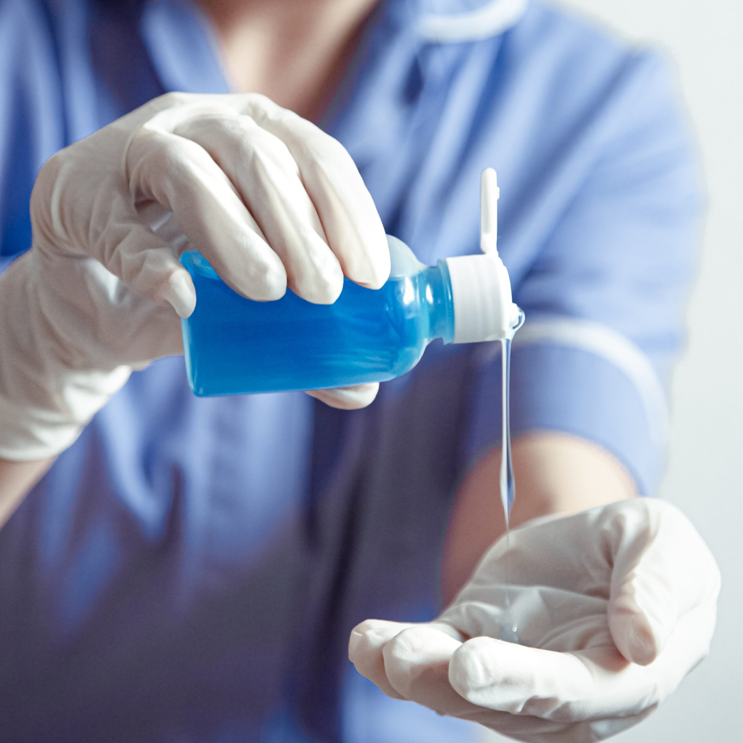 Doctor in a blue coat and protective gloves. The use of a disinfectant with gloves. Personal hygiene and virus protection concept.
