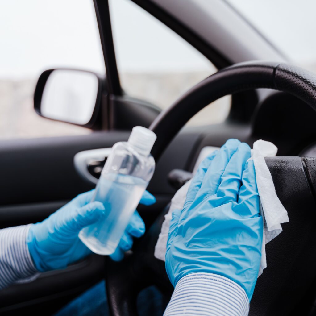 unrecognizable man in a car using alcohol gel to disinfect steering wheel during pandemic coronavirus covid-19